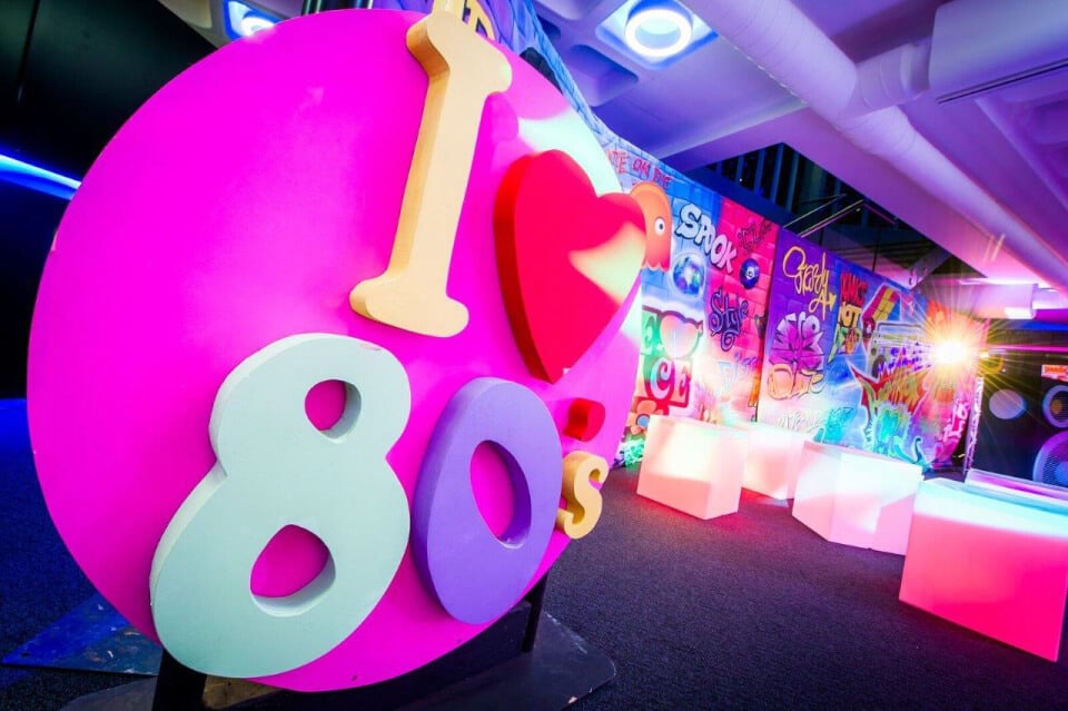 I heart 80's sign in bright colours with light up chairs in background freestanding props and decor graffitit wall art