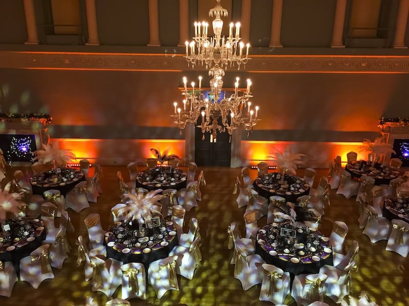 White and gold themed room from above with chandelier and gold chair covers white and gold feather table centres. gold chair sashes on top of white chair covers