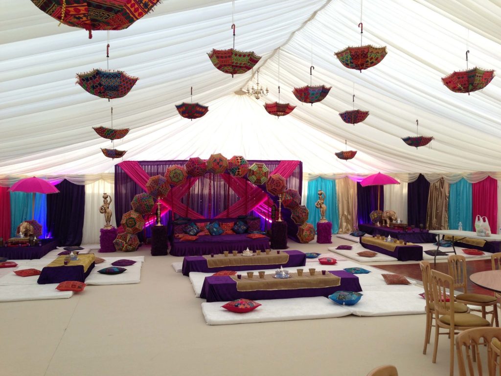 Morroccan themed event purple, pink, blue and gold colour scheme. Moroccan umbrella archway and ceiling decorations hanging from draped ceiling. Low purple tables with decorative tea set. Decorative gold sculptures and statues around the room