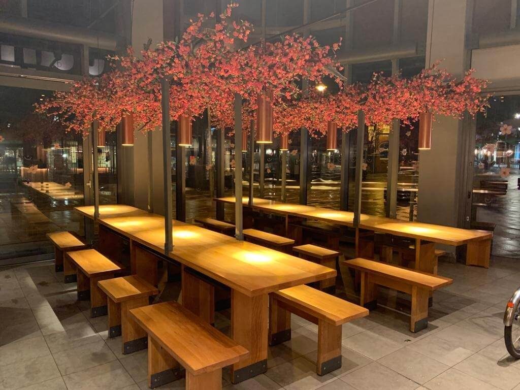 Wooden restaurant benches with red cherry blossom tree fake ceiling above tables