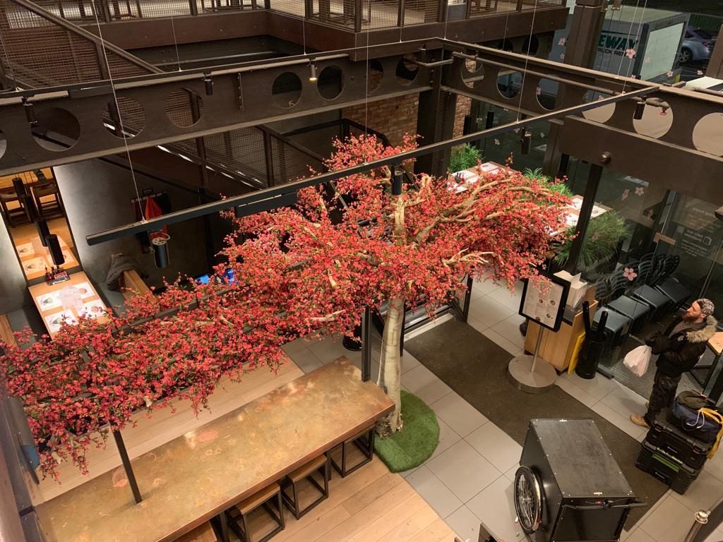 Overhead view of faux tree and red blossom flowers in restaurant above tables